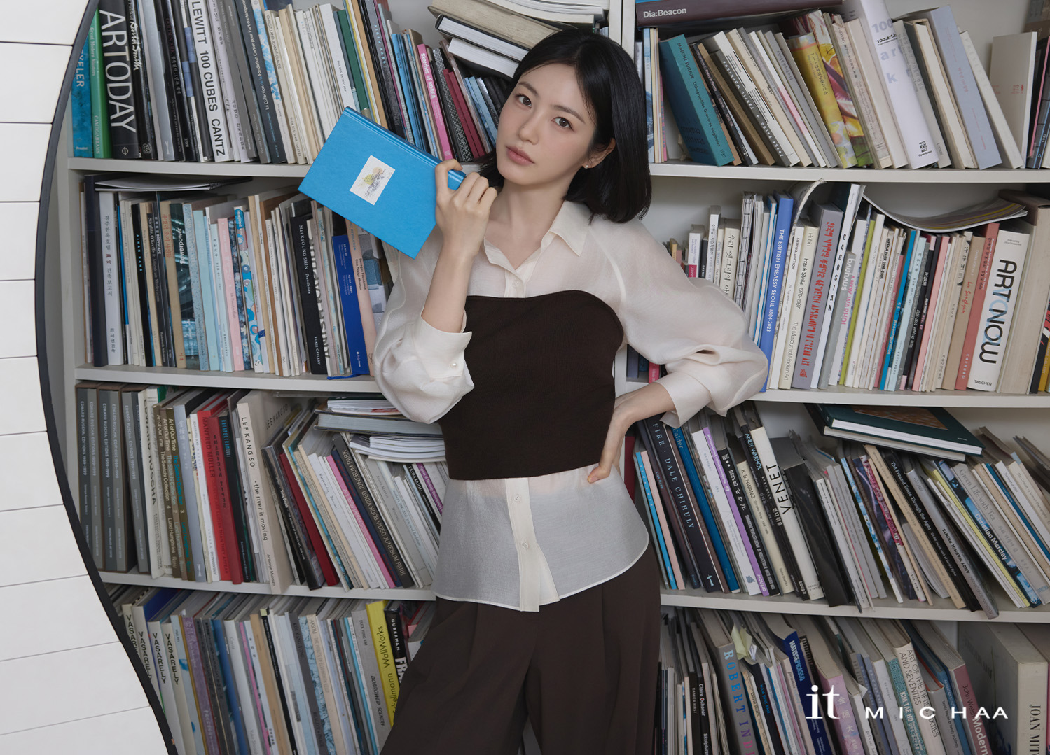 서재 배경에서 베이지 블라우스와 브라운 팬츠를 매치한 컷